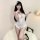 Woman modeling white lace open-crotch bodysuit with sheer floral pattern, ruffled hem, and feather hair accessory.
