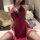 Woman wearing red lace-trimmed qipao-style lingerie set with thigh-high stockings, seated in elegant bedroom setting.