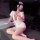 Woman in white nurse-themed lingerie set with red accents, posing seductively on a table in dimly lit room.