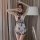 Woman wearing sheer butterfly lace sleepwear set with matching bralette, posing indoors near lamp and curtains.