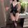 Woman wearing black lace fei niao moon gaze lingerie set with open-crotch bodysuit, holding champagne glass beside floral dec...