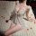 Woman wearing feiniao moonlit butterfly lace sleep set – sheer nightgown with embroidered wings, lying on rose-petal-strewn b...