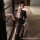 A woman wearing a black lace dress with deep v-neckline, high slit, and sheer fabric design, suitable for evening wear or sle...