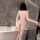 Woman wearing pink nightse bodysuit with open back, long sleeves, and thigh-high stockings in modern bathroom.