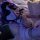 Woman wearing meiyoujia sensual couple lingerie set with black straps and fishnet stockings, lying on bed in purple lighting.
