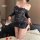 Woman wearing navy blue night silk lace bodycon mini dress with sheer sleeves and one-shoulder design, posing on bed with ros...
