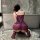 Woman wearing purple lace slip dress from night silk sensual lingerie set, kneeling by bathtub in elegant bedroom setting.