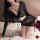 Woman wearing black sheer bodycon dress with cutouts and long sleeves, styled as sensual nightwear on fluffy rug with rose pe...