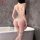 Woman wearing white lace thong bodysuit with garter straps, back view in bathroom.