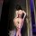 Woman wearing purple sheer lace nightsigh bodysuit with floral cutouts, backless design, and thigh-high straps in dimly lit r...