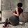 Woman in nightsigh nightsilk ol secretary outfit with bodycon skirt, holding a riding crop, posing by a bathtub.