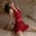 Woman wearing red deep v-neck sleep dress with sheer mesh back, posing on bed in plus size lingerie set.