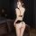 Woman wearing black lace bodysuit with open crotch and push-up design, shown from back in dimly lit room.