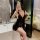 Woman wearing black lace-trimmed slip dress in bedroom, showcasing plus size sexy sleepwear with deep v-neck and sheer fabric...