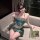 A woman poses elegantly on a couch wearing a luxurious green exotic strapless lingerie set, featuring intricate embroidery an...