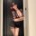 Woman in black floral lingerie set with bodycon skirt, lace mask, and red flower hair accessory.