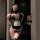 Woman wearing black and white lace lingerie set with blindfold, posing seductively in a dimly lit room.
