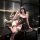 Woman in sheer black lingerie set with pearl details, posing seductively on a glossy surface.
