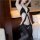 Woman wearing black pure temptation lingerie set for small bust, featuring cutouts and garter straps in a hotel room setting.