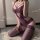 Woman wearing purple lace bodysuit with sheer panels and matching thigh-high stockings, kneeling on white rug beside wine gla...