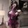 Woman wearing purple sensual bodysuit set with lace details, long gloves, and open-crotch design in a stylish room setting.