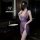 Woman wearing purple sheer lingerie set with deep v neckline and lace waistband, standing in modern bathroom.