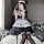 A woman poses in a maid costume featuring a black and white dress with lace details, sheer mesh apron, and adjustable straps,...