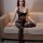 Woman wearing qingyege black sheer bodysuit and stockings set, elegant open-crotch lingerie on beige sofa.