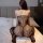 Woman wearing qingyege sheer lace lingerie set with open-crotch bodysuit and fishnet stockings, seated on bed.