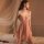 Woman in a pink qqny lingerie set with an underwire push-up bra and matching panty, standing beside a bed with sheer drapery.