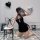 Woman in black retro lace cheongsam lingerie with sheer mesh back, kneeling beside stool with heart balloons.