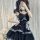 A person wearing a black and red rock gothic lolita dress with plaid accents, featuring a heart-shaped bow and layered ruffle...