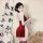 A woman poses elegantly in a red silk velvet qipao, featuring lace-up details and cut-outs. she holds a traditional fan, comp...