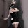 Woman in black bodycon dress with white lace trim, bunny ears, and gloves posing seductively in a doorway.