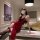 Woman in red lace lingerie set with thigh-high stockings, posing on a marble table in a luxurious bedroom setting.
