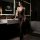 Woman in black seductive no-remove bodysuit set with lace details, posing in modern bathroom.