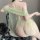 Woman wearing sheer green sensual hanfu lingerie set with mesh doudou and open back, seated on chair.