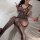 Woman in black lace lingerie set on white bed, featuring floral mesh bodysuit with strappy shoulders and fishnet stockings.