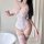 Woman wearing white lace bodysuit with garter straps and sheer stockings, standing beside a bathtub in elegant bedroom settin...