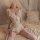 Woman wearing a white lace bodysuit with an open crotch and garter straps, posing seductively on a bed.