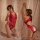 Woman modeling red lace bodysuit lingerie with sheer provocative design, no-remove style, in romantic bedroom setting.