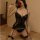 Woman in black lace babydoll bodysuit with garter straps and fishnet stockings, holding a red rose on bed.