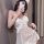 Woman wearing sheer lace bodysuit with low-cut bust and cut-outs, taking mirror selfie in white mesh mini dress.