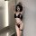 Woman modeling black suoqing sexy lingerie set with cut-out bralette, thong, and leg garter in modern room.