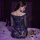 Woman wearing a blue lace bodycon skirt set with sheer sleeves, seated on a bed with rose petals for date night.