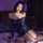 Woman wearing a blue lace bodycon skirt set with sheer sleeves, posing on a bed with rose petals for a romantic date night lo...