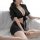 Woman in black sheer office secretary outfit with tied blouse and mini skirt, posing on bed for date night or role play.