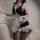 A woman poses in a black and white maid costume, featuring ruffled details and stockings, creating an elegant yet playful sce...