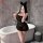 Woman in black sheer mesh lingerie dress with lace corset top and ruffled hem, posing by bathtub.
