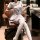 A stylish woman sits confidently in an office chair wearing a chic sailor uniform ensemble, featuring a white dress with blue...